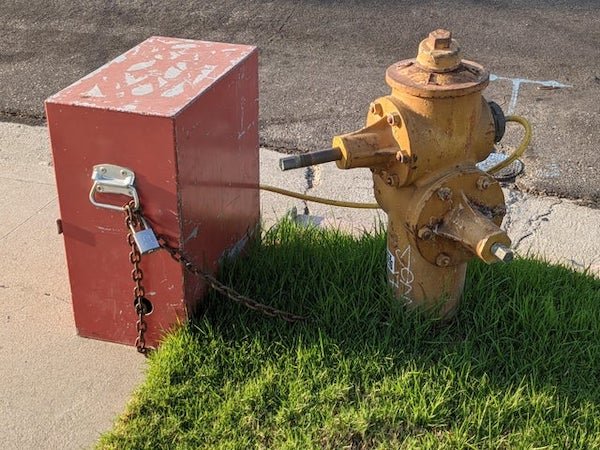 A hose coming from a fire hydrant to a metal box. What is this box?

A: Pressure logger. It records water pressure over time on a graph. This is an older one. Newer ones are electronic and can transmit the data wirelessly.