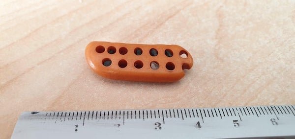 Small piece of eroded material with irregularly drilled holes. Found on a beach in Scotland.

A: This is an old, worn, toothbrush head.