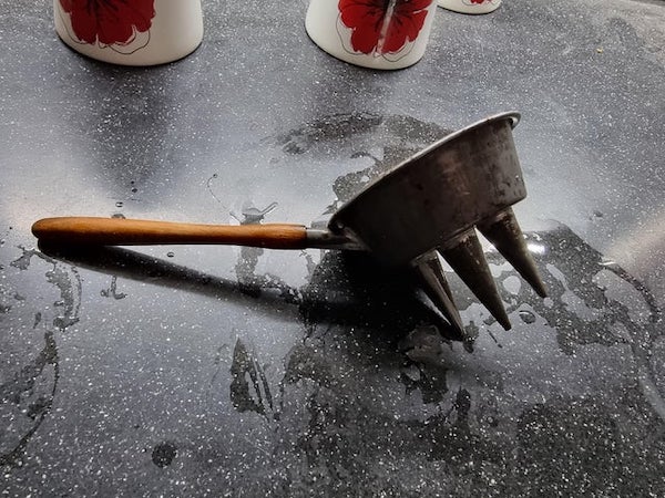 A kitchen utensil with a wooden handle, attached to a round metal cup with 3 spikes (with holes in)

A: It’s a funnel for making a portugese sweet called fios de ovos or egg threads.