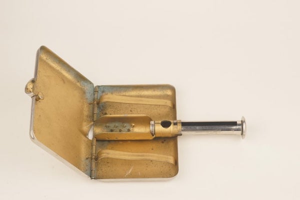 A pocket-sized metal box from 1924 with a plunger-ejector mechanism

A: Looks like a tobacco box with a contraption to fill the paper tubes to make cigarettes.