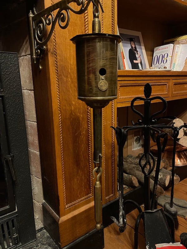 What is this thing hanging outside my fireplace. It seems to have gears inside of it, and pivots into the fireplace.

It’s a clockwork spit turner for turning a roast or other meat automatically.