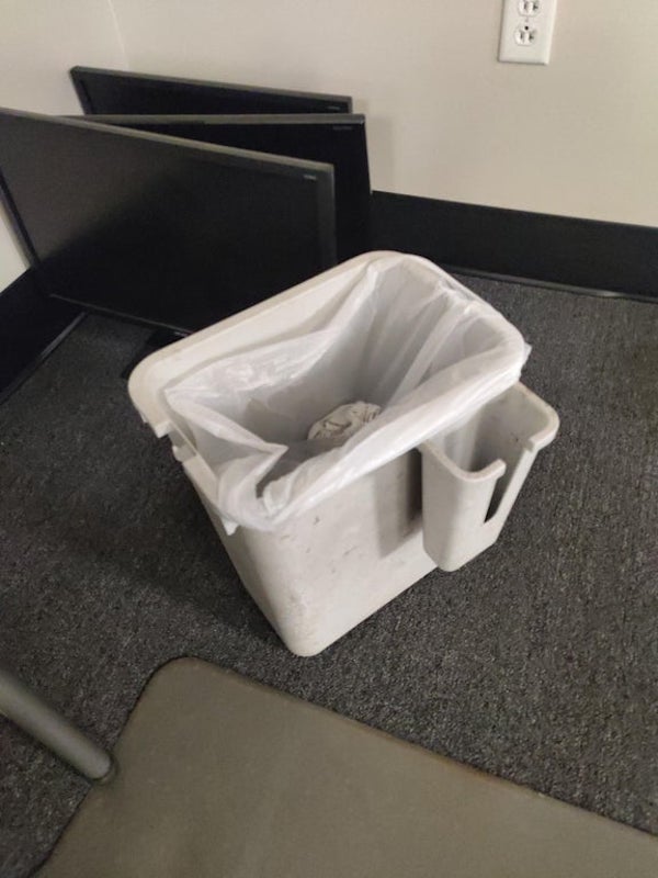 What is this thing on the side of the garbage can.

A: That’s not a bin, it’s a waste paper collector for a shredder. Have a look at the top, it’s designed to slide into place. Usually the other smaller bit is hung inside the paper collector under the bag, and it usually holds a brush and lubricant for the mechanism.