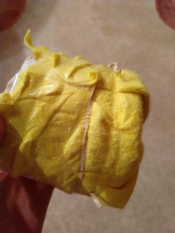It’s a toilet paper roll wrapped in a yellow cleaning cloth, that is attached by gummy strings and clear tape. The cloth is stuffed into the roll on one end.

A: We called these splooge tubes… For the smoking.