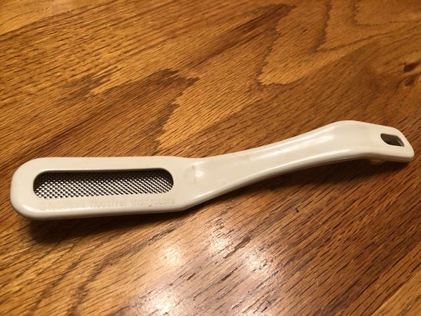 Found in a kitchen cupboard. Hard plastic tool with dimpled metal section on the end, rough but not very sharp, looks like it might be removable. The metal section is lower down leaving a gap above it. Says ‘stainless rostfrei inoxydable’ on it. About 19 cm long (7.5 inches).

A: This is a hard skin remover. For your feet. True story. The fact you found it in a kitchen drawer is a concern.