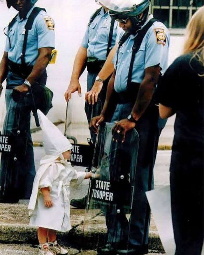 fascinating photos form history  - ‘No One Is Born Racist’ Photograph By Todd Robertson. A Boy Dressed In A Kkk Robe And Hood, Curiously Touches The Shield Of A State Trooper During A Kkk Rally | Gainesville, Georgia, 1992