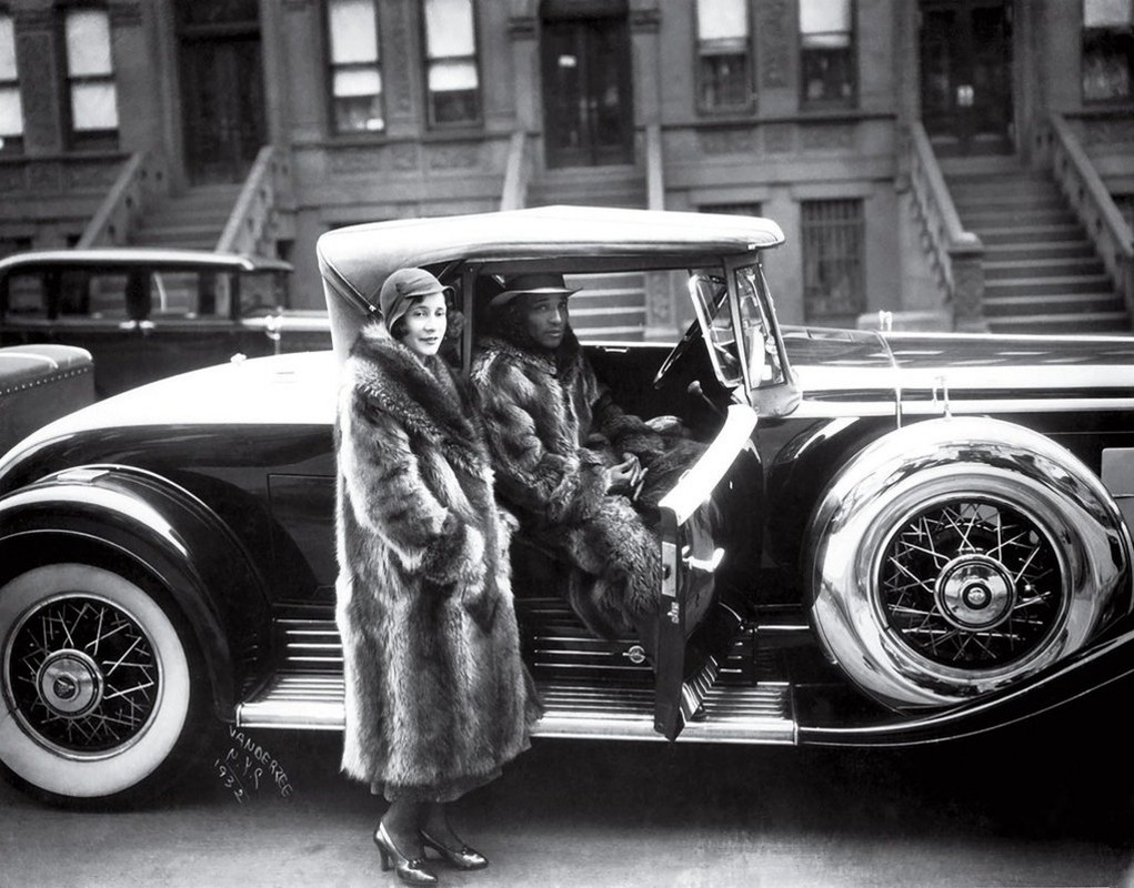 A Harlem couple wearing raccoon coats with a Cadillac 1932