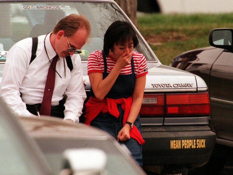Columbine teacher Judy Greco sitting on a car with a bumper sticker that reads “Mean People Suck” after escaping the school. (April 20, 1999)