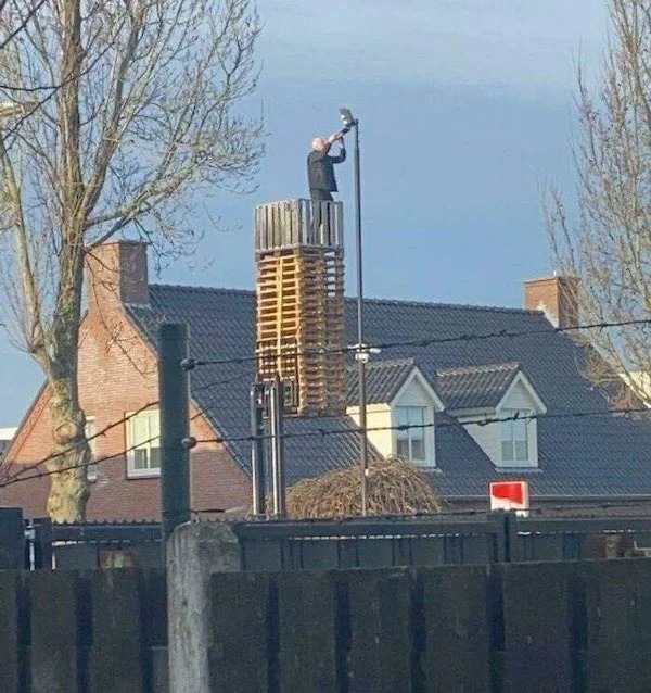 Just a man on a stack of pallets raised by a forklift changing the bulb on a street light.