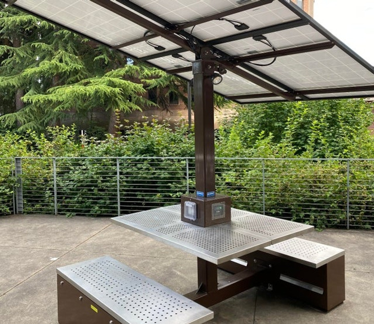 “A table with a solar panel as a sunshade that doubles as a charger for the ports at its base”