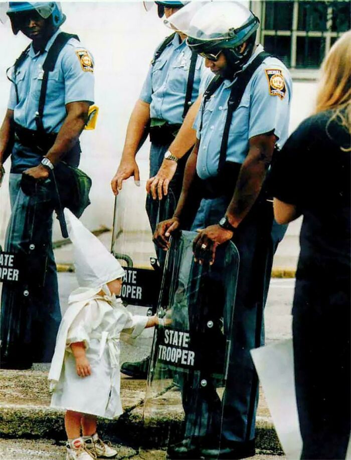 A Ku Klux Klan Child And A Black State Trooper Meet Each Other, At A Klan Rally Protest In Gainesville, GA (1992). Innocence is mixed with hate. The toddler approached the trooper, who was holding his riot shield on the ground. Seeing his reflection, the boy reached for the shield.