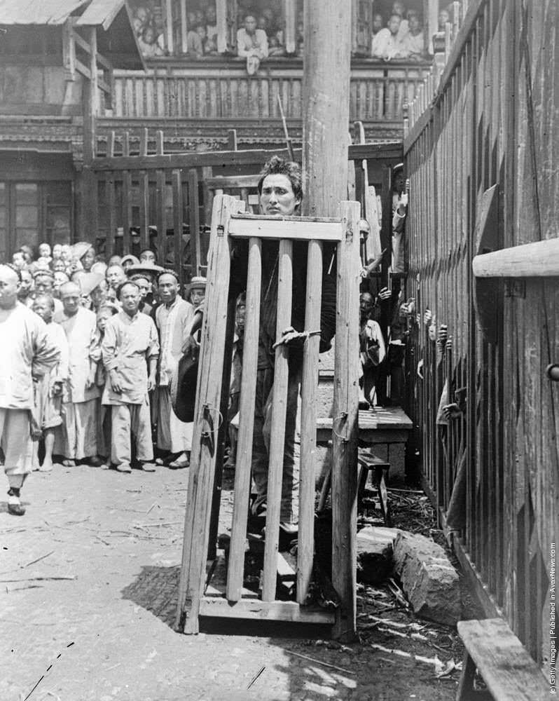 A river pirate who killed at least 6 people including gouging a victims eyes out is awaiting his execution in China in 1900.He is standing on stones or wood beams. Each day, 1 will be removed as his head is secured on the top. Eventually he will have noth
