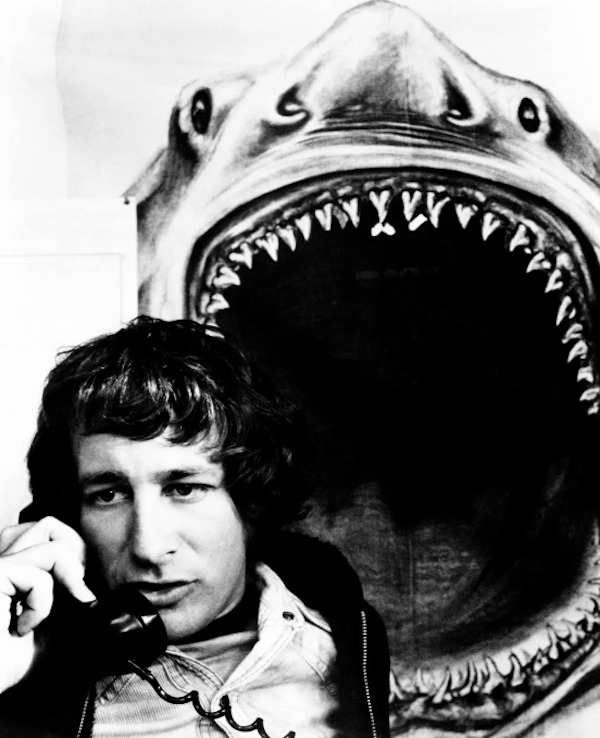 A young Steven Spielberg making a call while a shark ominously watches in the background on the set of Jaws (1975):