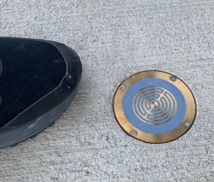 “A small cover on the sidewalk with a metal pattern, foot for scale”

Answer: "It’s a rain and frost/ice detector. A small current is on the 2 metallic circles, they are not touching and are isolated against each other. When raindrops connect the 2 metals, the small current is amplified or switched, so it can trigger a pump or close windows that are fully open at that time and rain or snow won’t damage things."