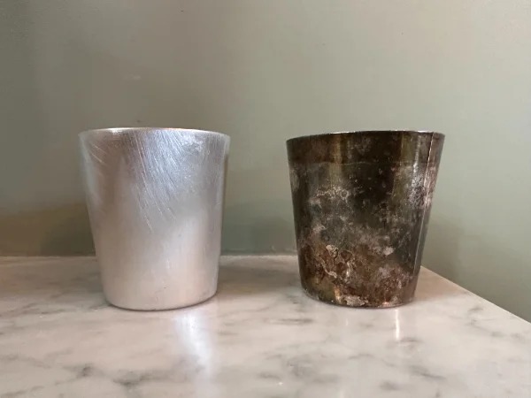 “A cleaned silver shot glass next to its tarnished sibling.”