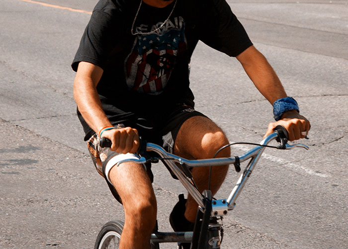 An adult man riding a child's BMX bike down the center of the road.