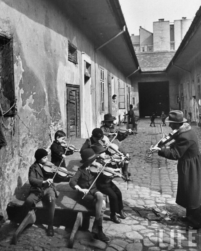 Gypsy Children Being Taught To Play The Violin In A Courtyard Of One Of The Poorer Houses. Budapest, Hungary, 1939. 