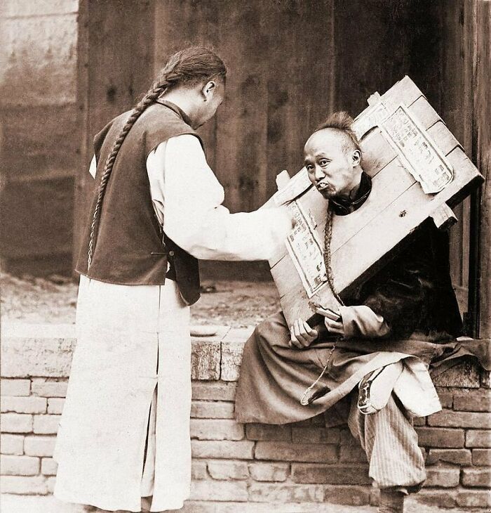 Chinese Man Feeding A Criminal In A Cangue, 1905.