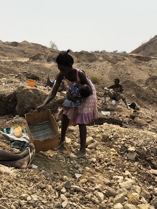 This teenager in DR Congo putting her baby into a cardboard box, so she can dig cobalt used for batteries