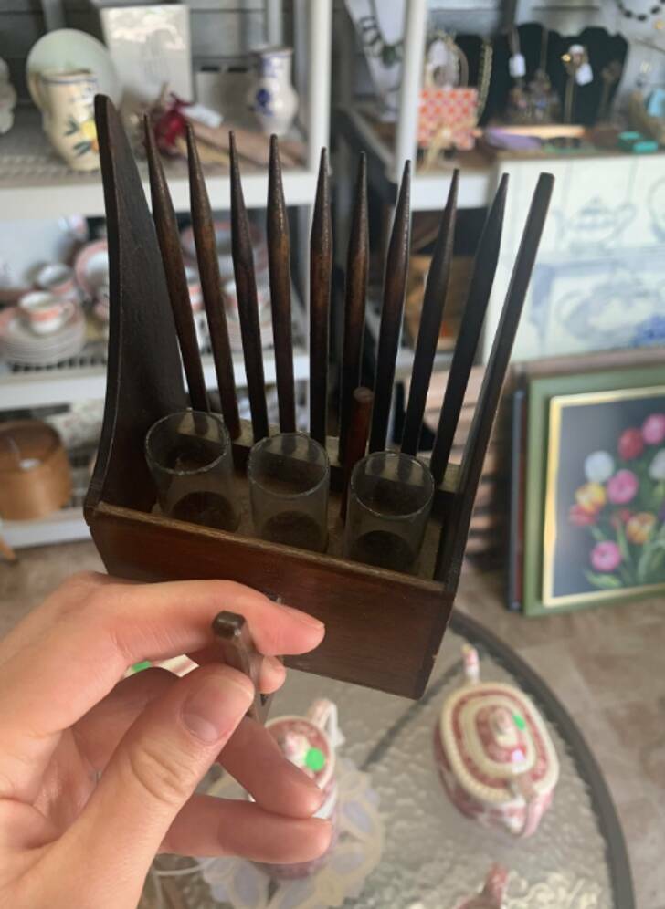 “A wooden tool with comb-like prongs, 3 glass vials positioned behind the prongs, and a small handle behind the vials.”

“That looks like someone took a berry picker and turned it into a decorative bud vase.”