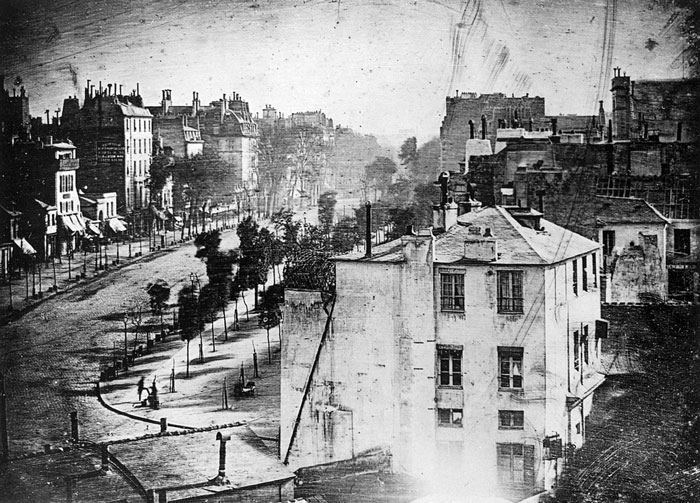 Louis Daguerre made history by capturing the first photograph to feature a human being. The photo depicts a street scene in Paris, but if you take a closer look at the bottom left corner, you’ll see two people — one getting their shoes polished by the other. Since they were standing still during the long exposure time, they could be captured while the rest of the busy street was not.