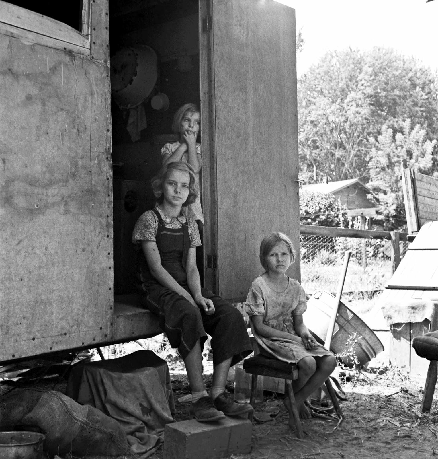 The oldest girl seated in the doorway of the house trailer cares for the family. Yakima Valley, Washington 1939. photo by Dorothea Lange