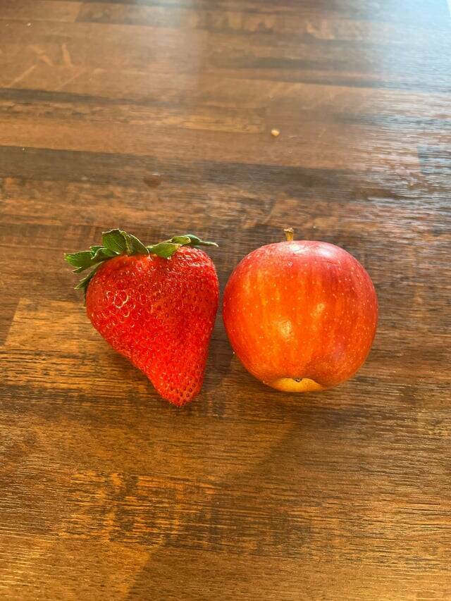 "Really big strawberry next to a really small apple"