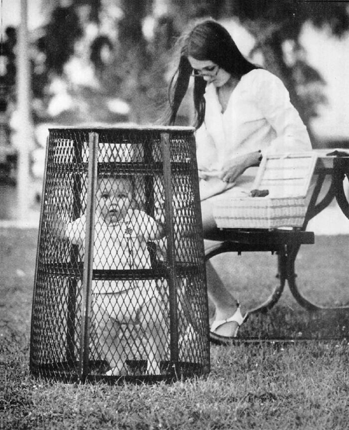 A Mom Uses A Trash Can To Contain Her Baby While She Crochets In The Park, 1969