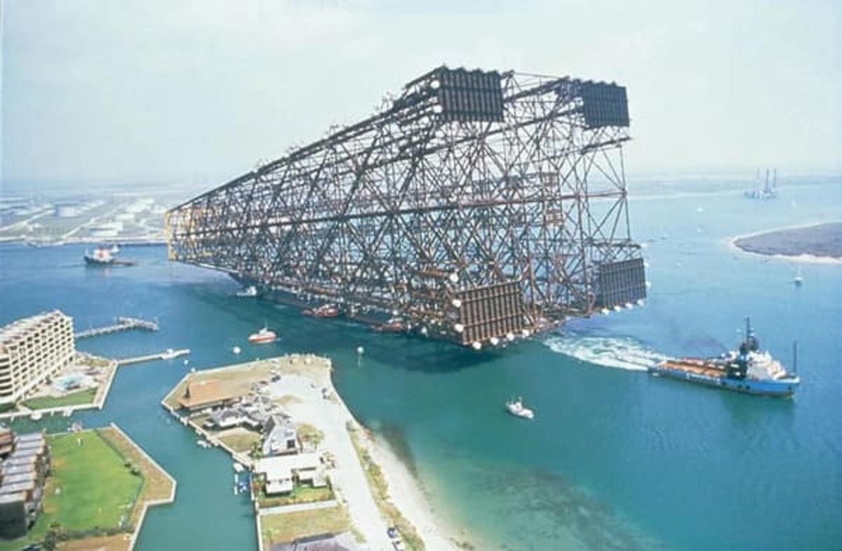 “Oil rig platform being towed into the sea. The platform itself is dwarfing the luxurious hotel on the left”