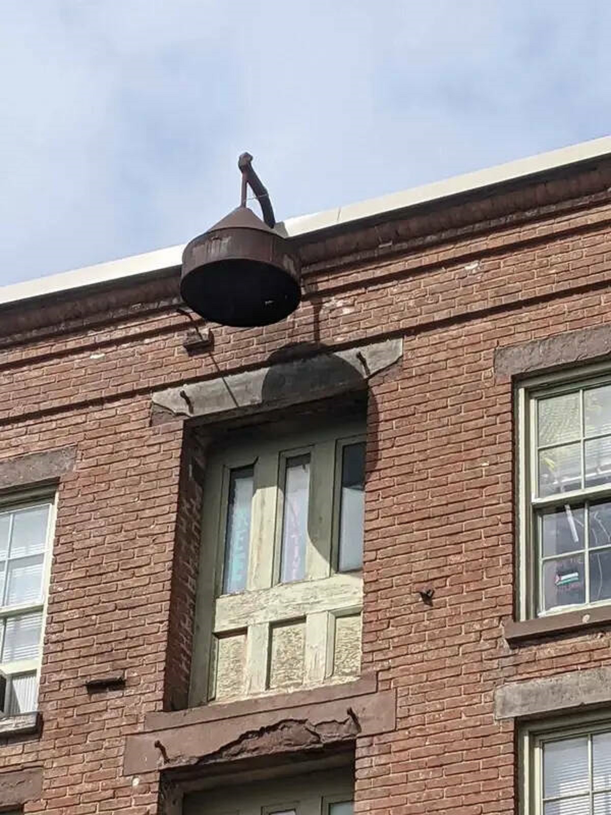 "This bell-like structure at the top of a Victorian-era brick building"

A: “It’s a hook used to hoist furniture to the upper floors of the building. A pulley is hung from it to assist. The bell shape is likely just to protect from rain.”