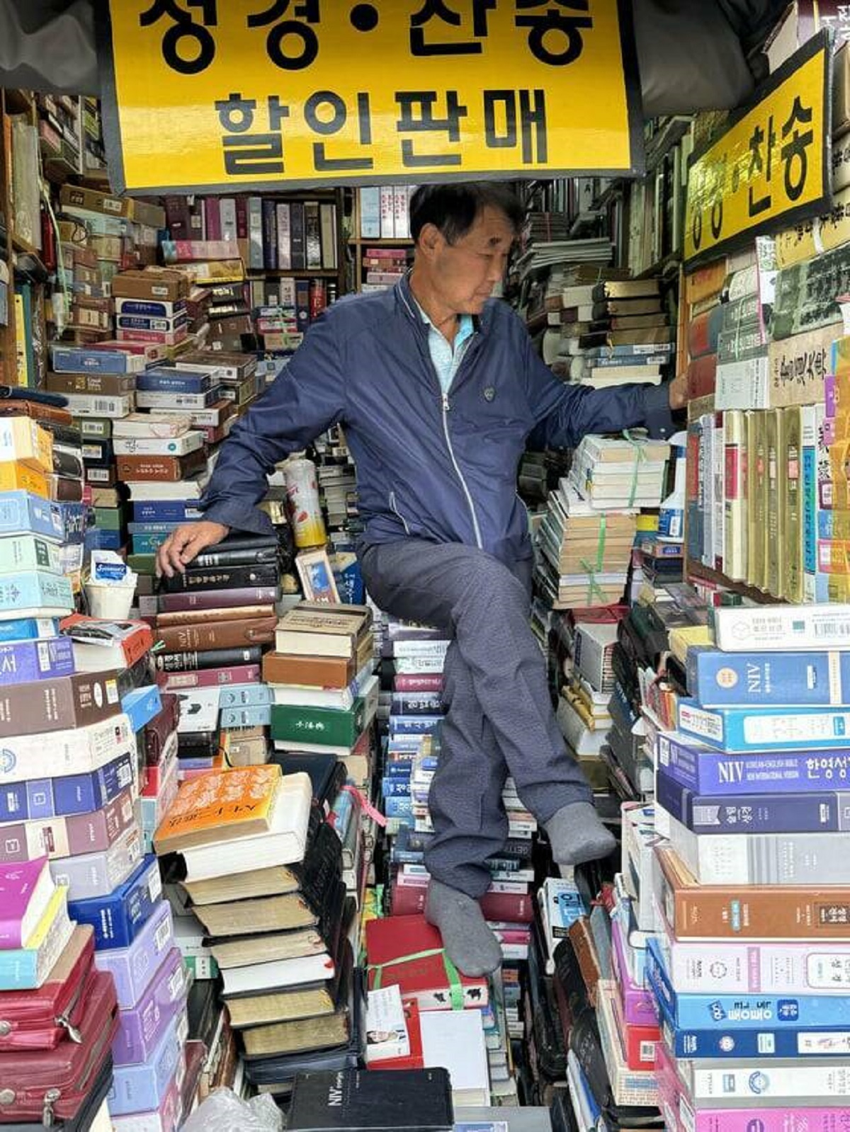 "Man sitting on his throne of books at a market in Seoul, Korea"