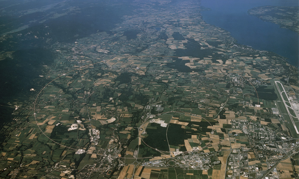 Aerial view of CERN and the surrounding region of Switzerland and France. Three rings are visible, the smaller (at lower right) shows the underground position of the Proton Synchrotron, the middle ring is the Super Proton Synchrotron (SPS) with a circumference of 7 km and the largest ring (27 km) is that of the former Large Electron and Positron collider (LEP) accelerator with part of Lake Geneva in the background.