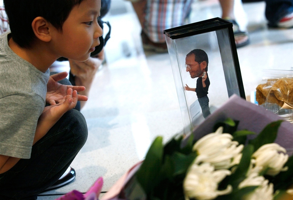 A boy looks at a figure of Steve Jobs next to flowers laid in his tribute at an Apple store in Hong Kong, China.