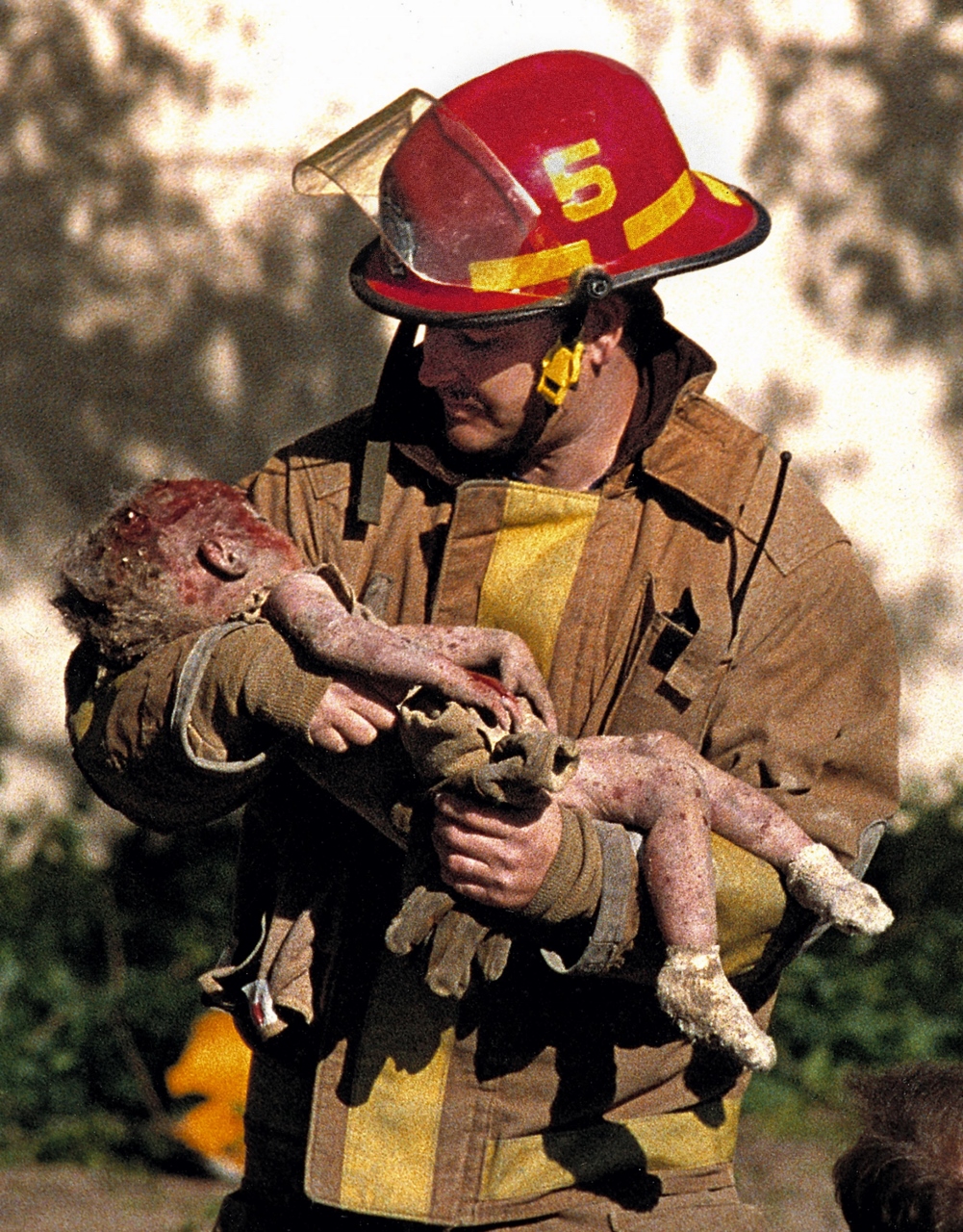 1996:  Charles Porter – “Oklahoma City Bombing.”  On April 19, 1995, Porter was at work in downtown Oklahoma City when the building he was in was rocked by an explosion.  Porter grabbed his camera and ran toward the explosion, seeing injured people, broken glass and debris along the way.
When Porter reached the Alfred P. Murrah Federal Building, he saw a police officer hand something to a firefighter.  The firefighter turned and Porter saw he was carrying an infant.  Porter took one shot.
The explosion injured more than 500 people and killed 168, including the child in Porter’s picture, Baylee Almon, who celebrated her first birthday the day before.