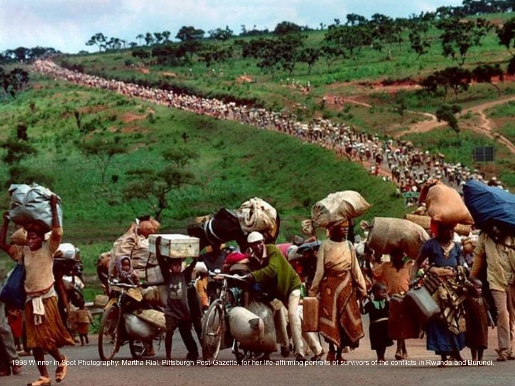 1998:  Martha Rial – “Trek of Tears: An African Journey.”  The line of refugees reaches to the horizon, victims of the centuries old warfare between Africa’s Hutu and Tutsi tribes.  Most are women and children.  Many are hungry.
Said Rial: “The stream of refuges you see here had been walking for almost 24 hours.  The previous evening they heard word that the Tanzanian government was going to force them to leave.  They were trying to flee, to go deeper into the bush.  They were forced back by the troops into Rwanda.  the group is led by a handful of militia guys.  Men who are the leaders in the communities.  They may or may not be wanted for genocide.”