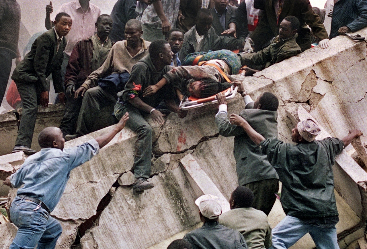 1999:  Sayyid Azim, Jean-Marc Bouju, Dave Caulkin, Brennan Linsley, John McConnico and Khalil Senosi – “Series of photos depicting the aftermath of the bombing of the US Embassies in Kenya and Tanzania. 
In this picture, rescue workers carry Susan Francisca Murianki, a U.S. Embassy office worker, from the rubble of a collapsed building next to the embassy in Nairobi on Aug. 7, 1998, after terrorist bombs exploded minutes apart outside the U.S. embassies in the Kenyan and Tanzanian capitals. In Nairobi alone more than 200 people were killed and about 4,000 wounded.  The Pulizter was awarded for this portfolio showing both the horror and humanity triggered by the bombings.