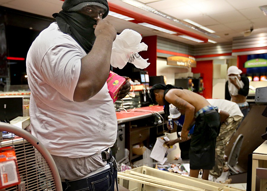 2015 Picture 3:  A looter armed with a gun in his waistband steals items from a QuikTrip after riots broke out at the end of a candlelight vigil for Michael Brown. The store was later set afire.