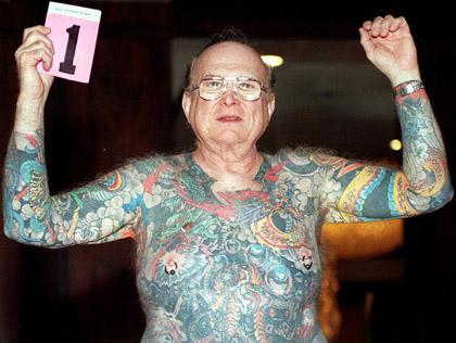 pierced and tattooed old man holding up a card with the number 1 on it