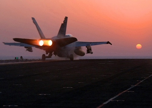An F/A-18 Hornet taking off of the flight deck, afterburners at full.
