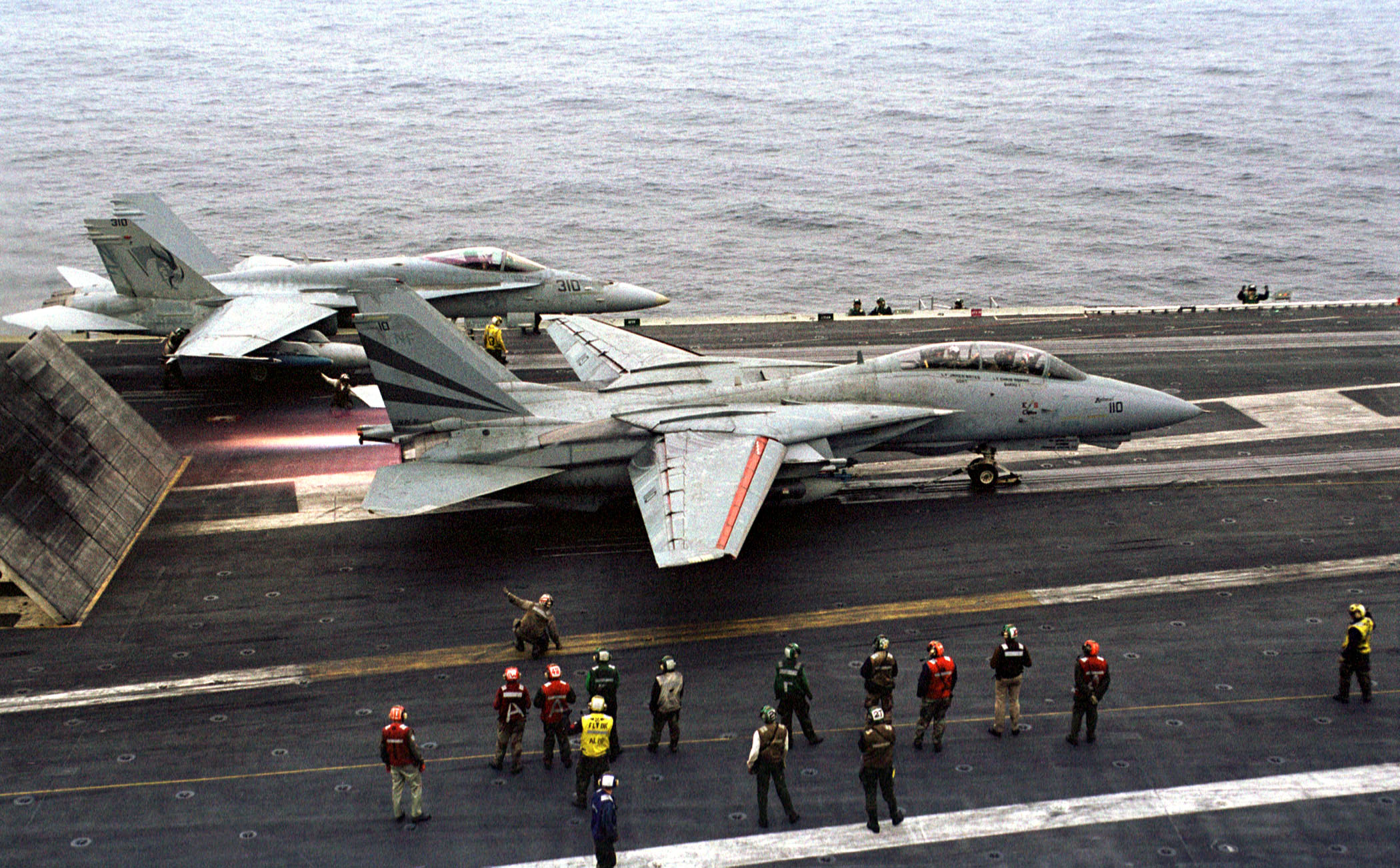 An F-14 Tomcat Fighter pumps up the afterburners, preparing to launch from the waist of the USS Kitty Hawk.
