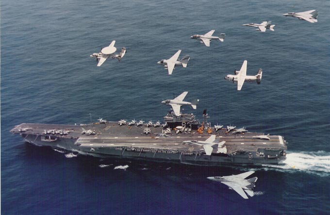The Kitty Hawk steams through the sea, shadowed by an E-2C Hawkeye surveillance plane, one S-3 Viking, two EA-6B Prowler Electronic Warfare jets, two F/A-18 Hornet fighters, two F-14 Tomcat fighters, and a single C-2 CoD cargo plane..