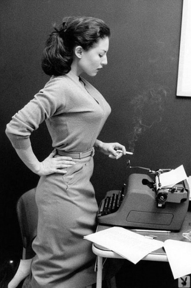 A secretary peering down at her typewriter holding a cigarette