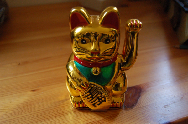 Maneki-Neko. This Japanese fella is supposed to bring fortune. Some claim the way the hand is risen must be always the same while others says it doesn't matter; one hand grabbed a symbol of fortune the other is a greating.
This is popular knowledge but there are many types of this cat: white means innocence, black keeps away demons, golden brings home money, red one keeps diseases at bay, and a pink one gives you luck for your love life. Japanese say that if maneki-neko rises his right hand he gives money and luck, if left he gives many guests and customers, some mane them with both hands in the air but the Japanese find them distasteful.