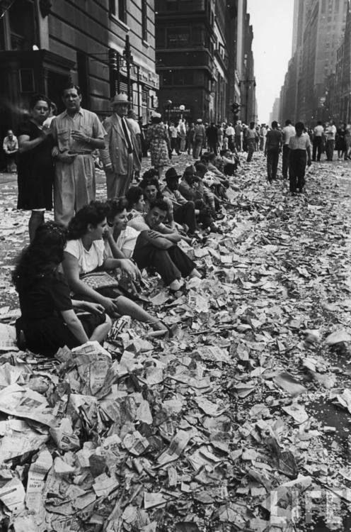 People sitting on curb among confetti and paper after celebrating the end of WWII in NYC, 1945.