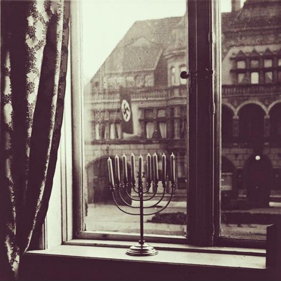 A Menorah sitting inside a house while a Nazi flag is right outside, 1931.