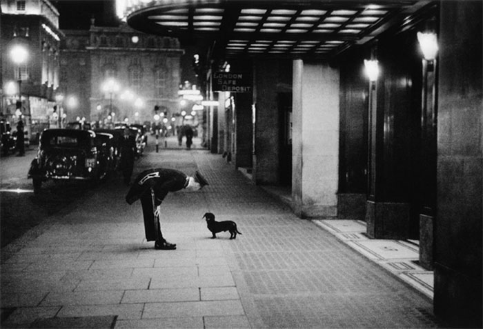 A hotel Commissionaire talking to a small dog in Piccadilly Circus, London, 1938.