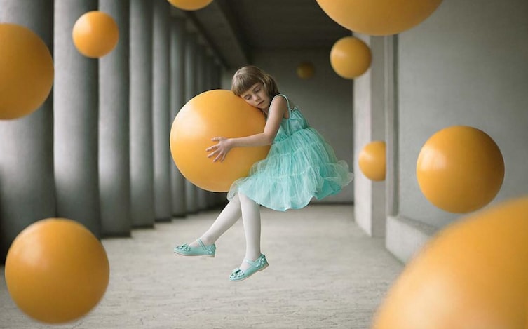 A young girl defies gravity gripping a yellow ball.   Open Enhanced category.