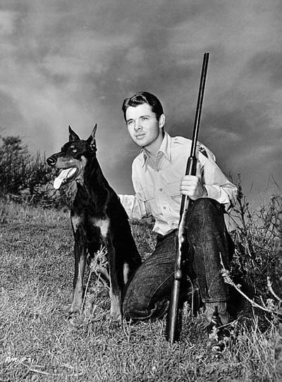 Audie Murphy poses with his pet Doberman while hunting for a magazine shoot sometime in the mid 1950s.