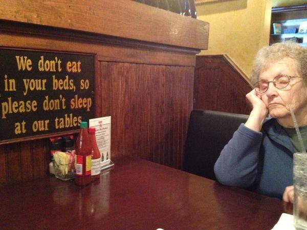 Woman passing out in a booth despite sign against doing such things.