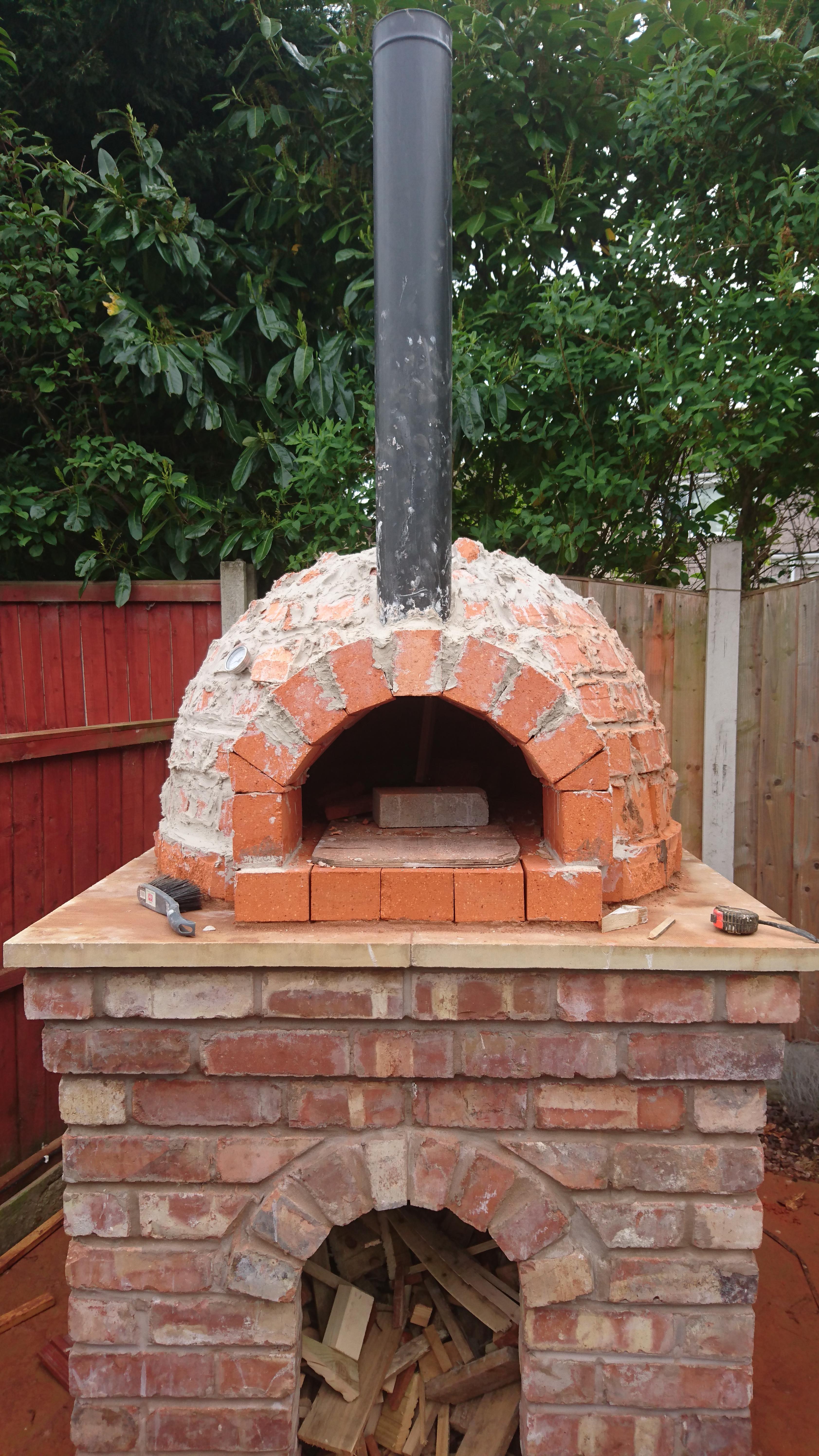 "Now the whole thing needs a thick coat of fire cement to bond it all together. I collected whatever off cuts/pieces of fire brick I had left over and filled as much of the joints in between the bricks as possible. Here I removed the arch former to reveal the door opening. I also managed to rescue the beloved trammel tool as a memento."