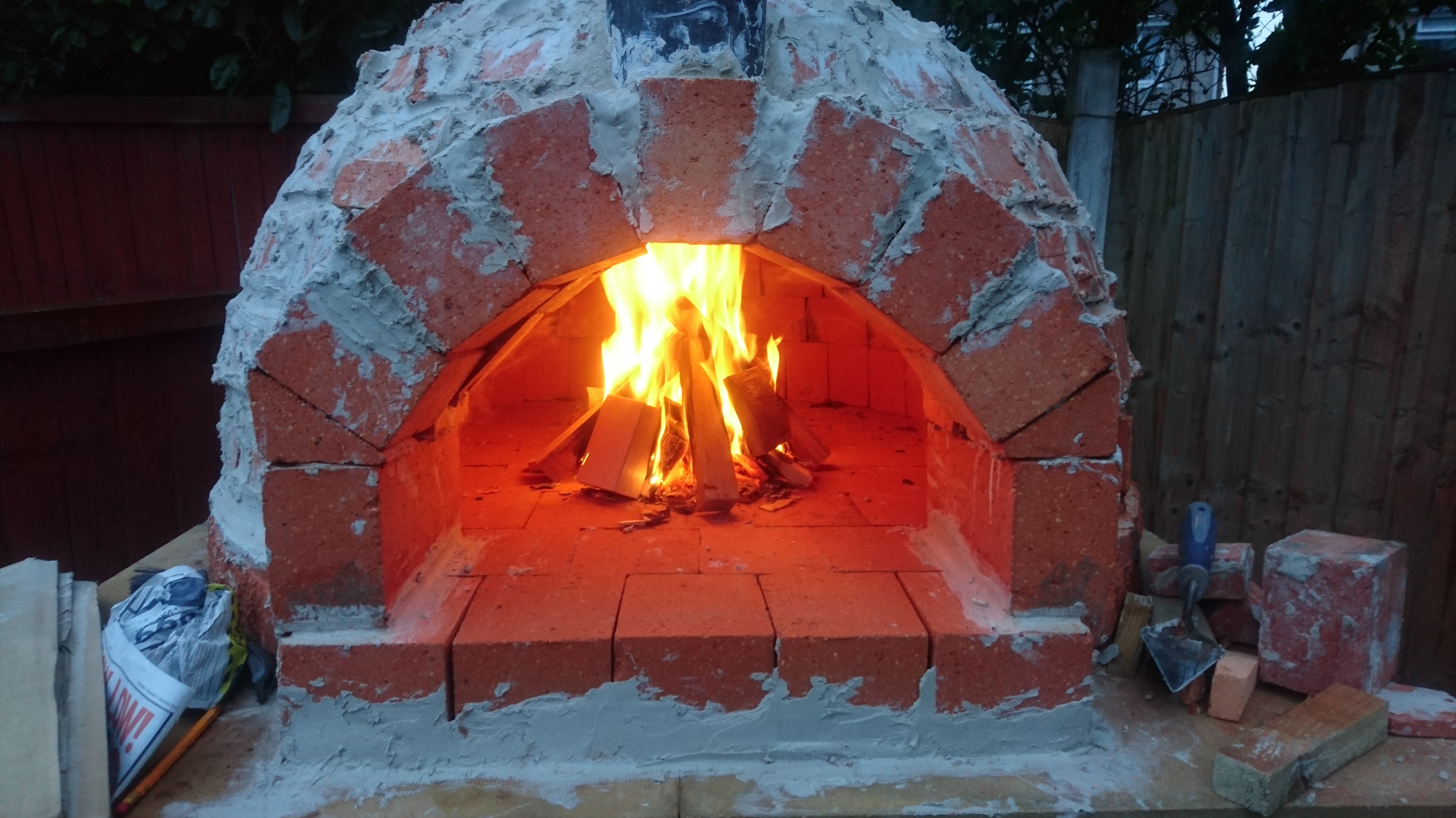 "First fire to cure the cement. Curing the oven is essential and will take around 5 days of building small fires and gradually increasing them. However, this is just the first one. It's crucial to cure the oven to make sure it sets the cement. It's important that nothing is cooked in there until the whole thing is complete, due to steam escaping from food which may effect the cement setting properly. Very frustrating but worth the wait."